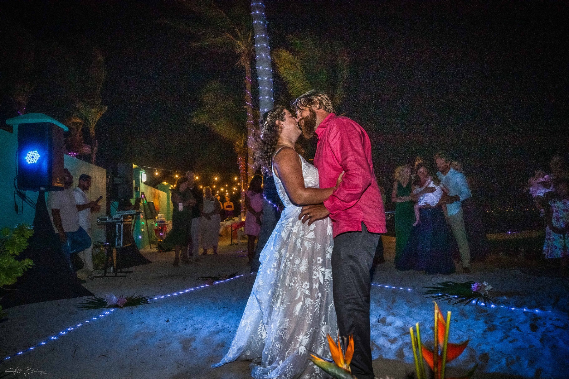 Bride and groom share a first dance kiss on the sand under string lights