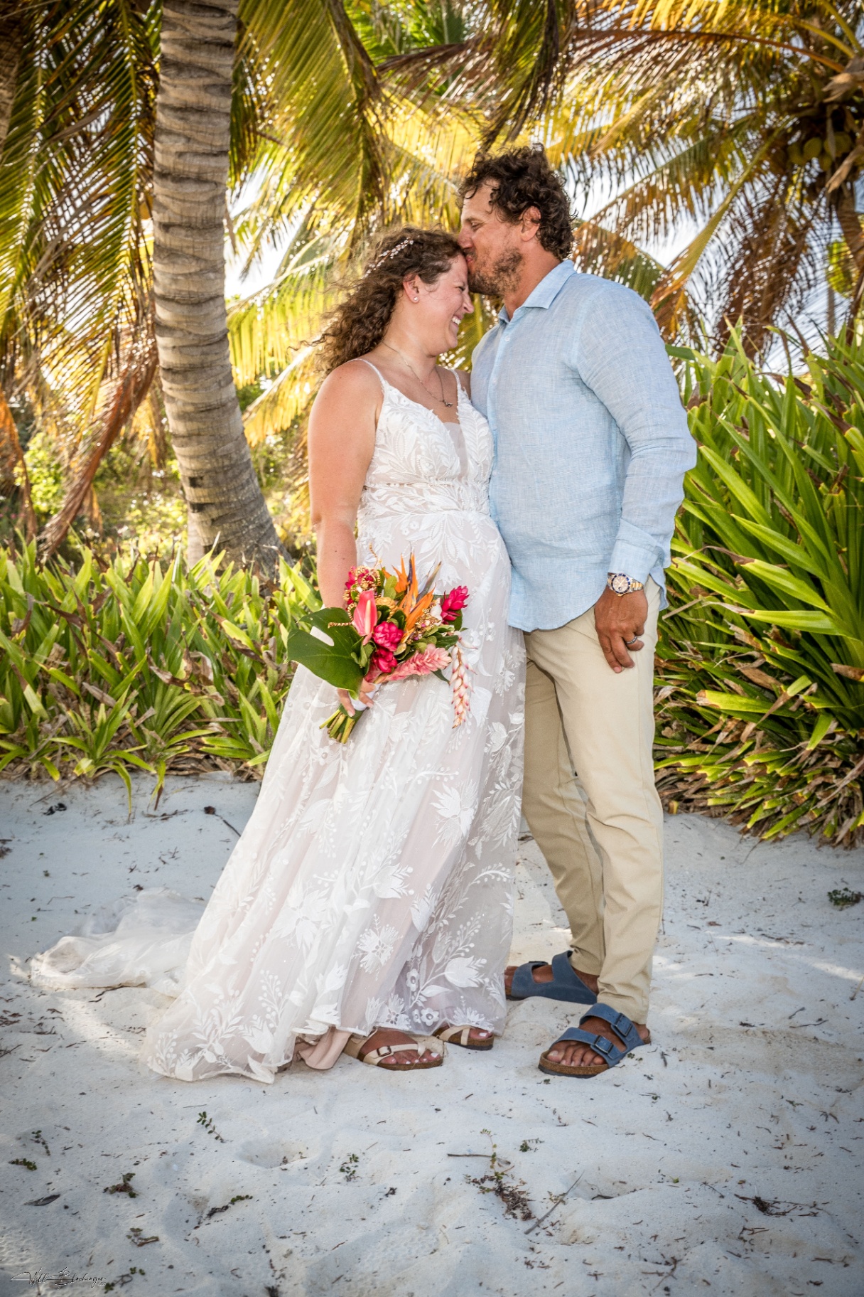 Bride and groom with tropical bouquet beneath palms on the Playa Blanca beach