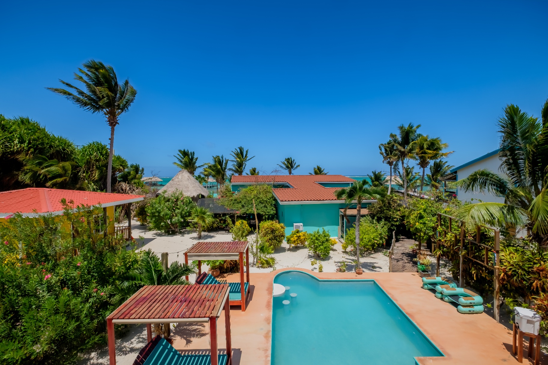 Aerial of pool, palapas, and turquoise sea beyond