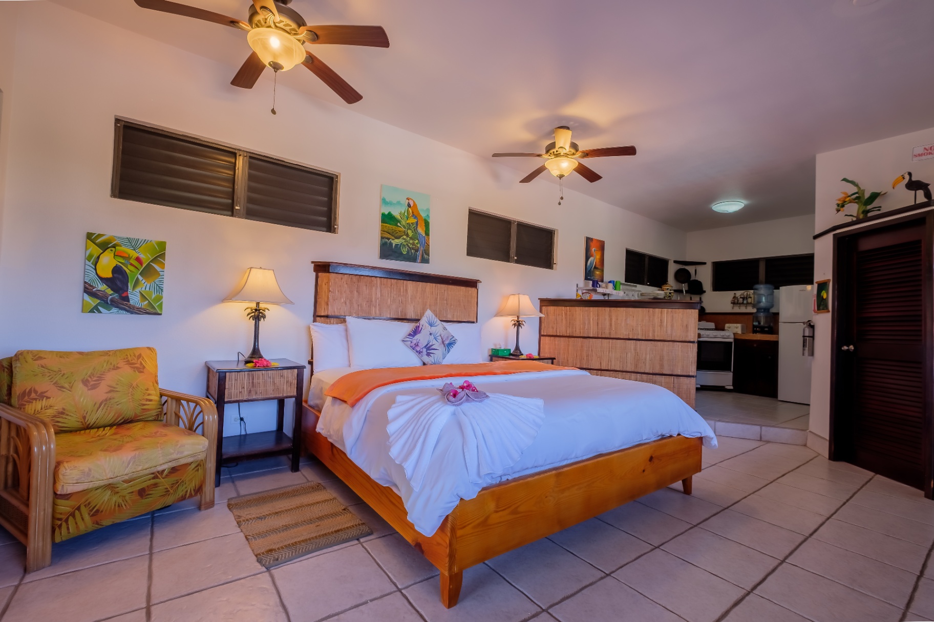 Studio with king bed, tropical art, and kitchenette beyond