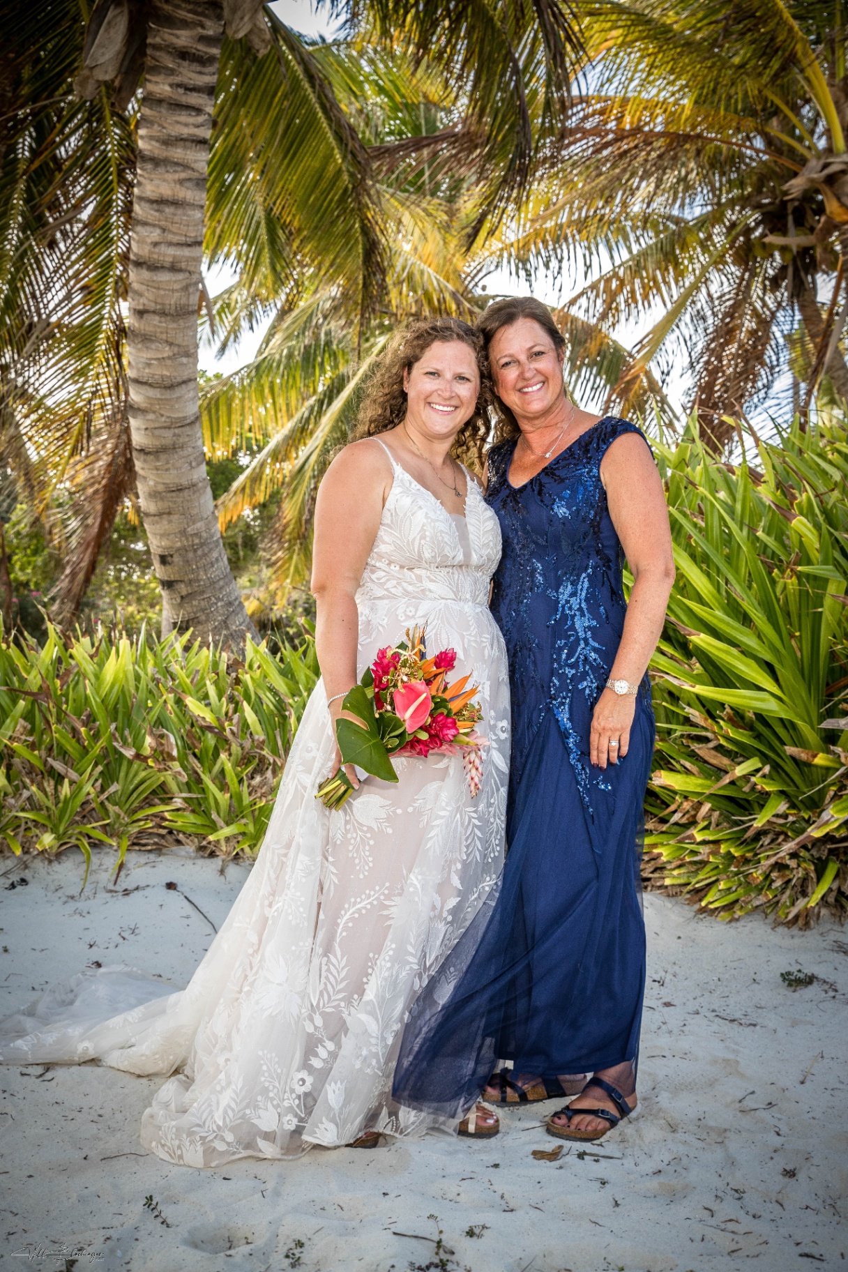 Bride and her mother posing together under the palms with a tropical bouquet