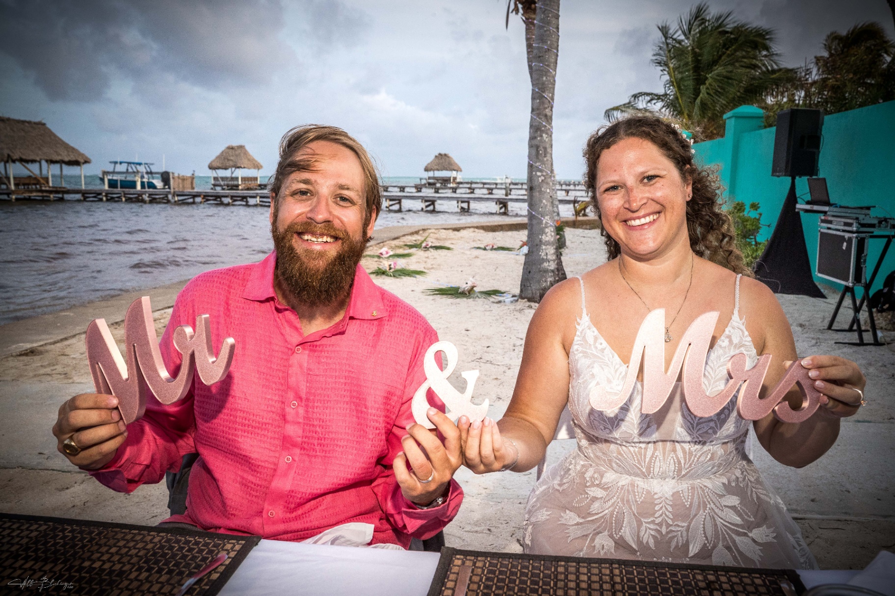 Bride and groom holding Mr & Mrs signs in front of the Playa Blanca beach and dock