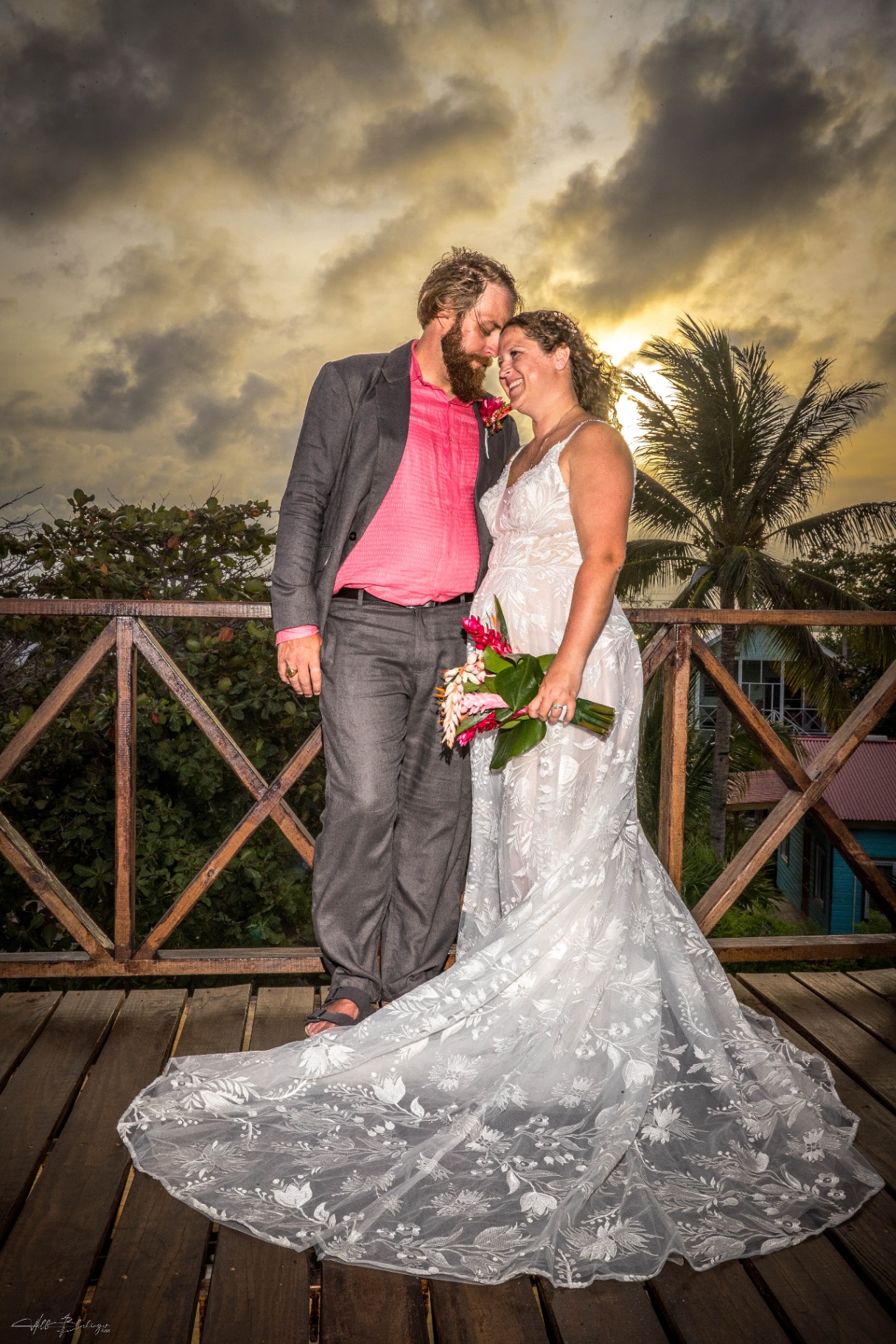 Bride and groom smiling forehead to forehead at sunset while holding a tropical bouquet