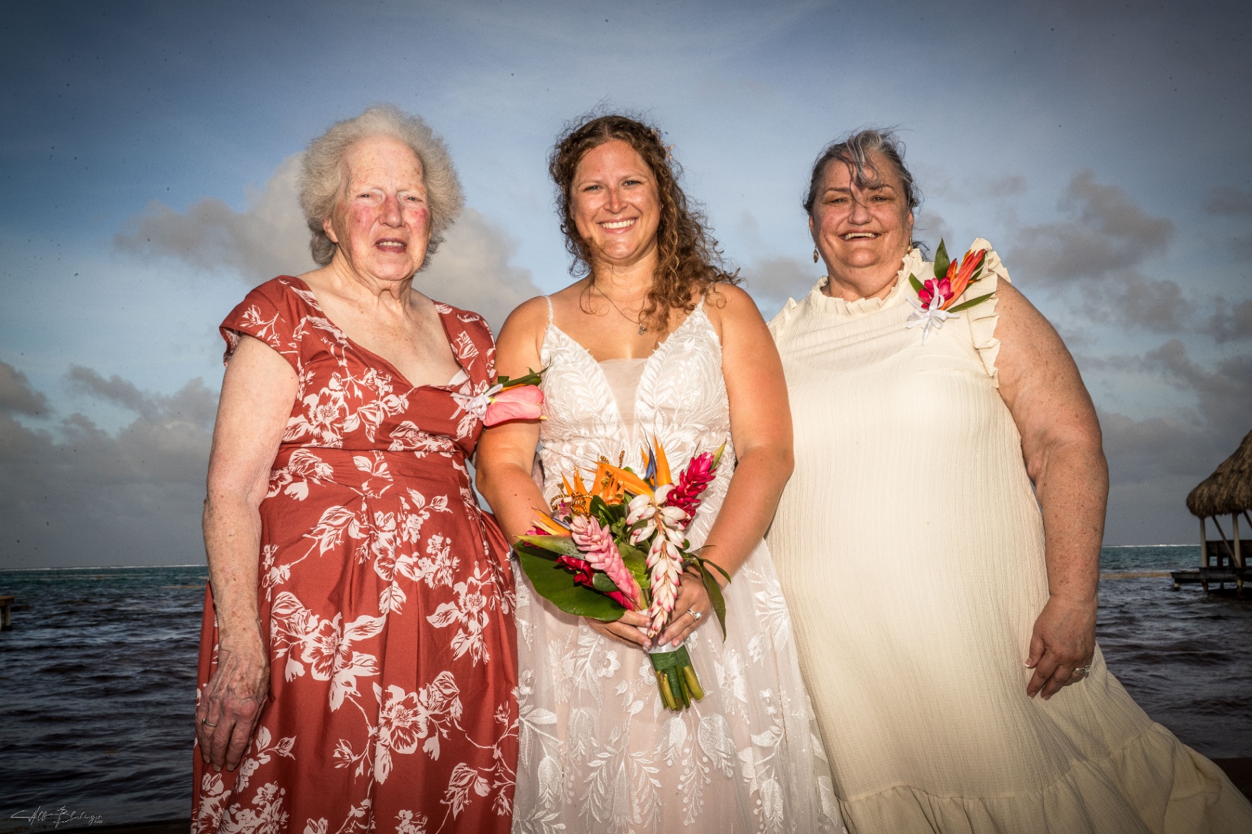 Bride posing with two women from her family at the water's edge after the ceremony