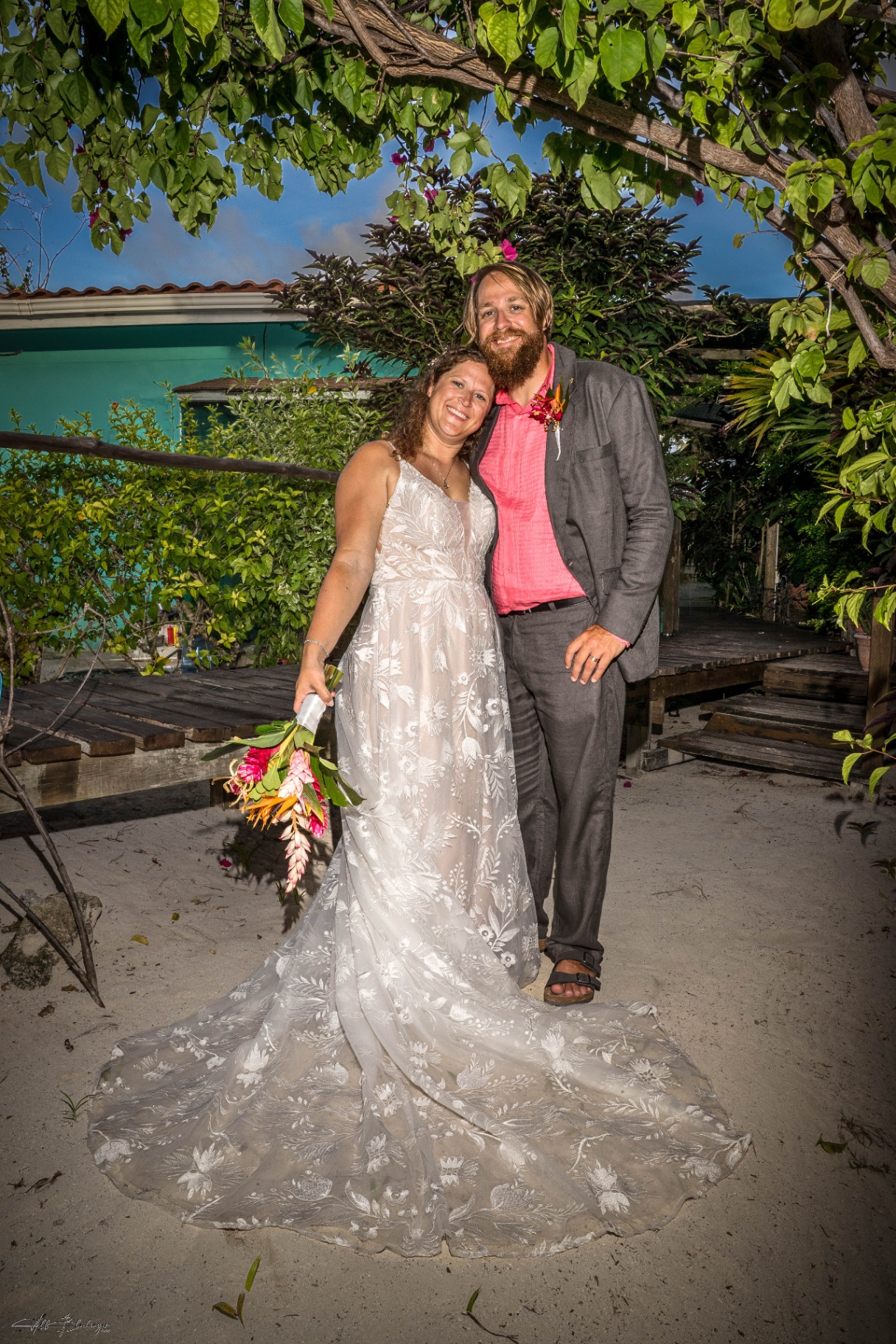 Bride and groom standing together in the sandy courtyard framed by tropical greenery