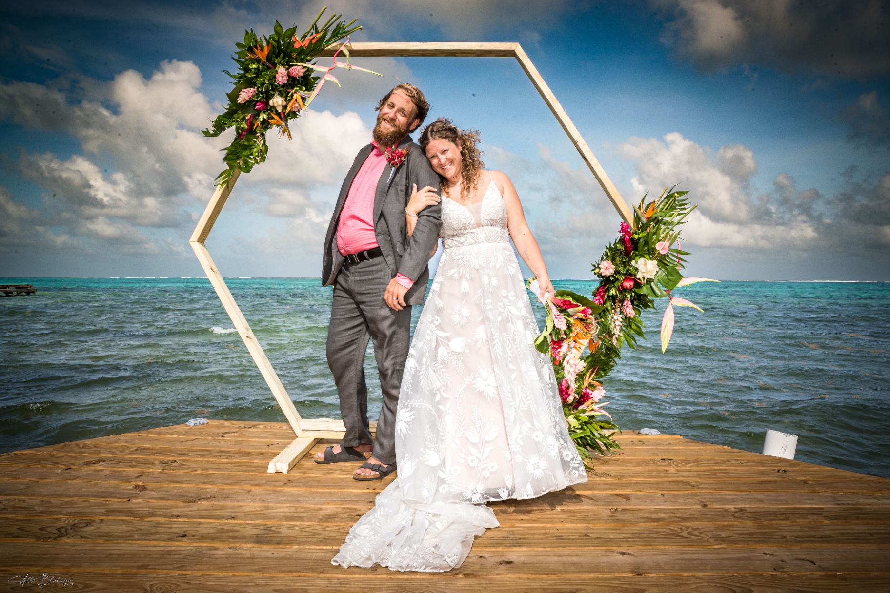 Bride and groom posing inside the hexagonal floral arch on the dock with the reef behind them