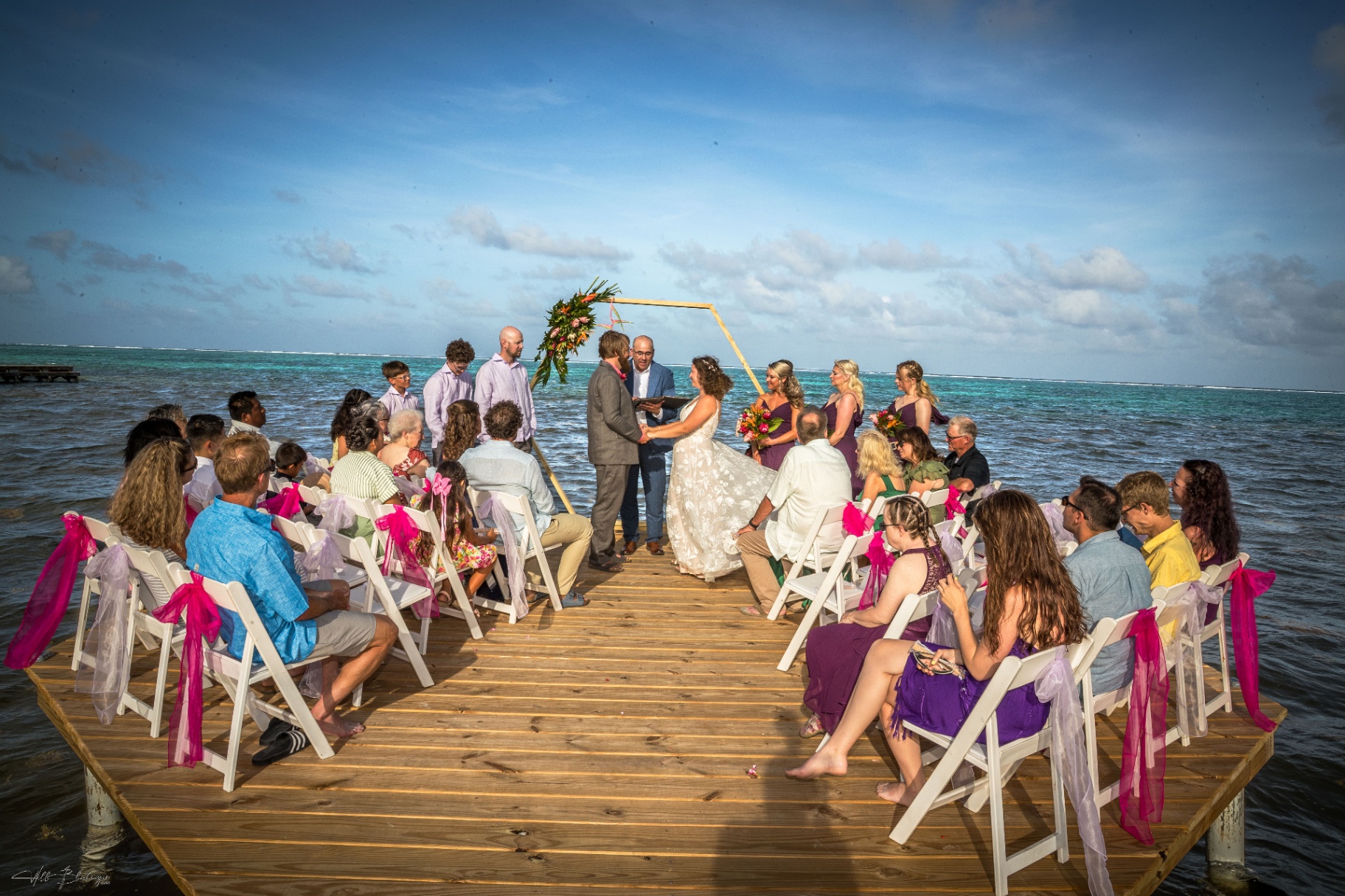 Wedding ceremony on the overwater dock with guests and Caribbean reef behind the couple
