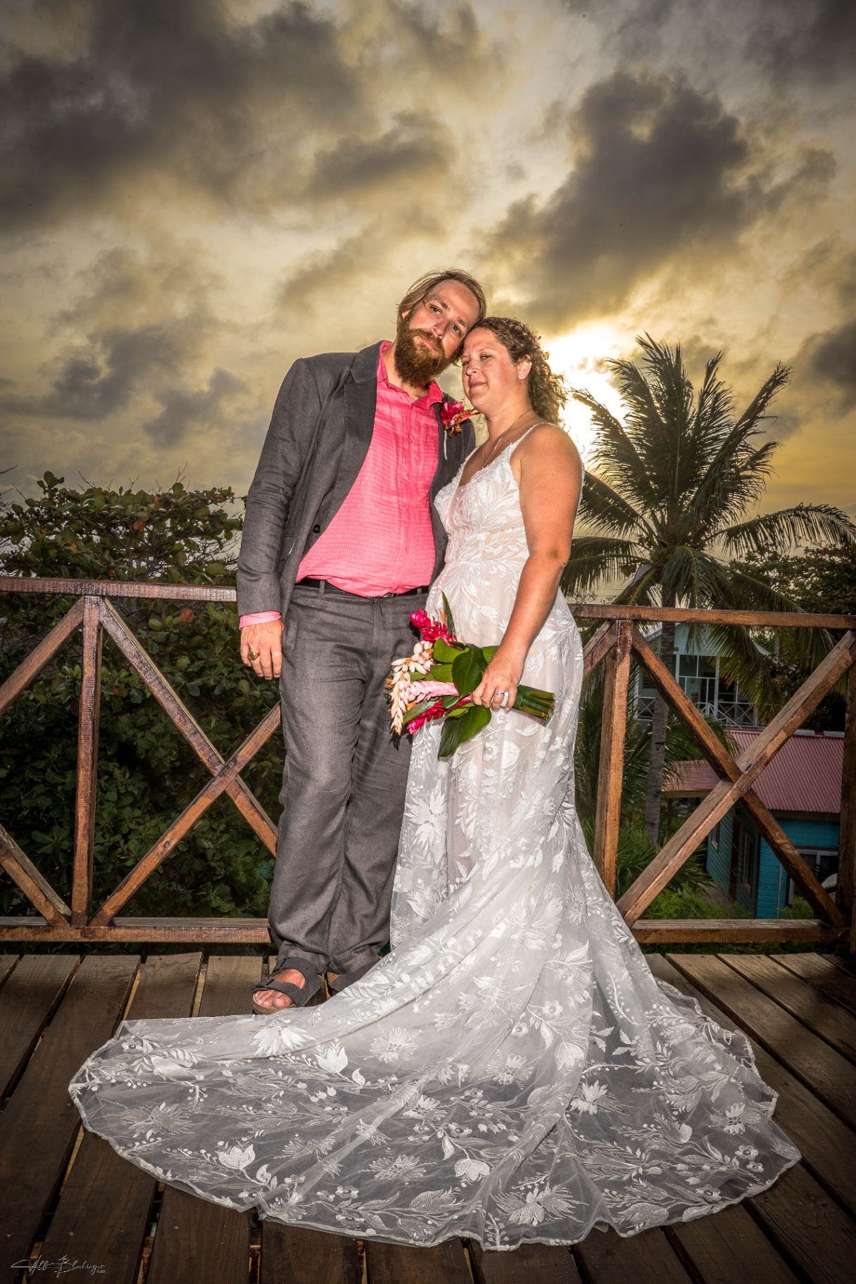 Bride and groom leaning together for a sunset portrait with palms and glowing clouds behind them