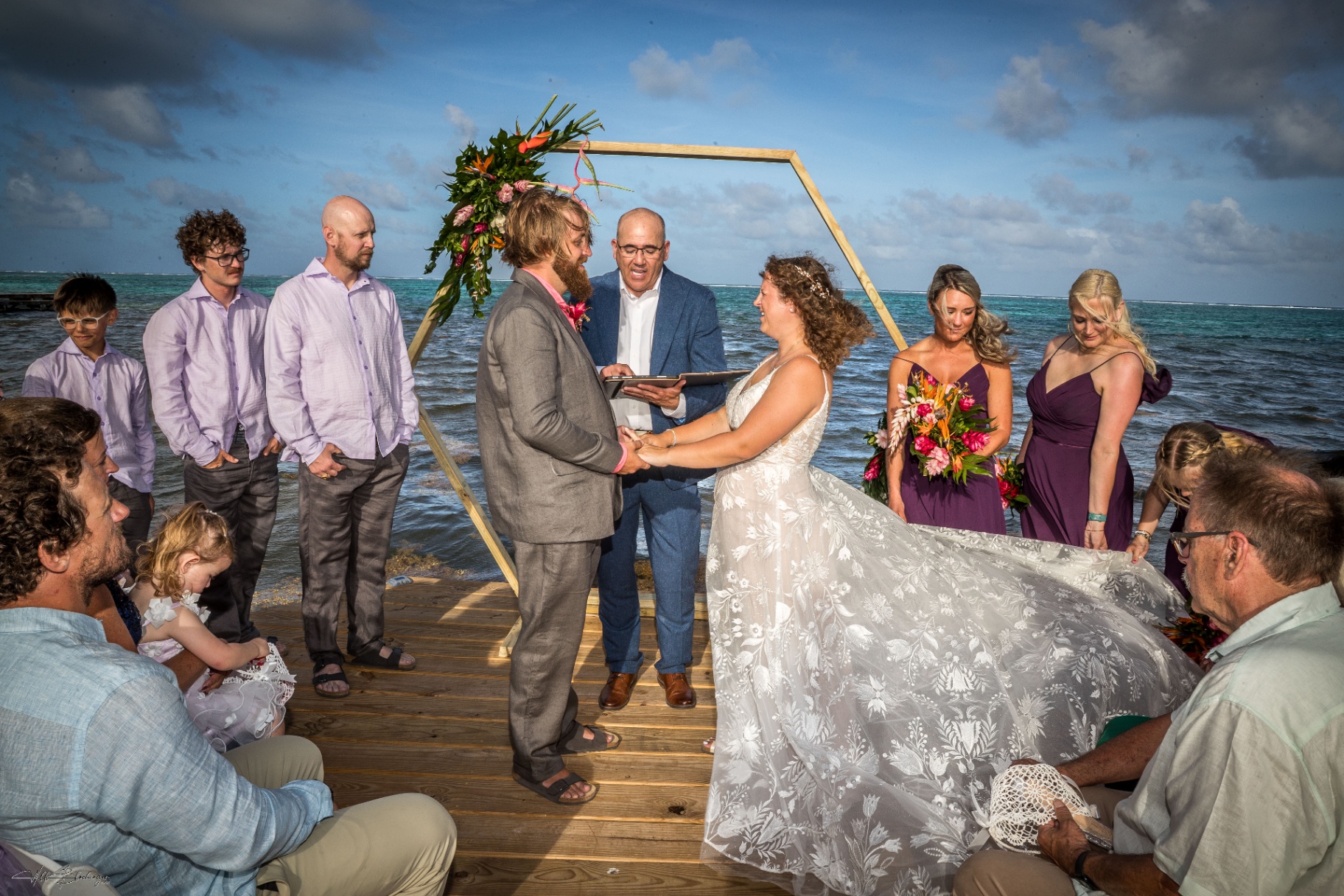 Bride and groom holding hands during their dock ceremony with bridesmaids and family gathered close