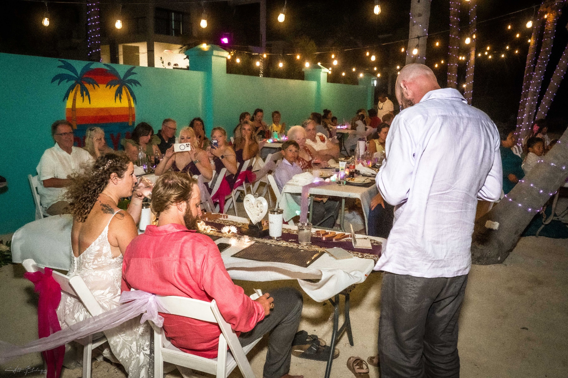 Best man delivering a toast at the candlelit beachfront reception under string lights