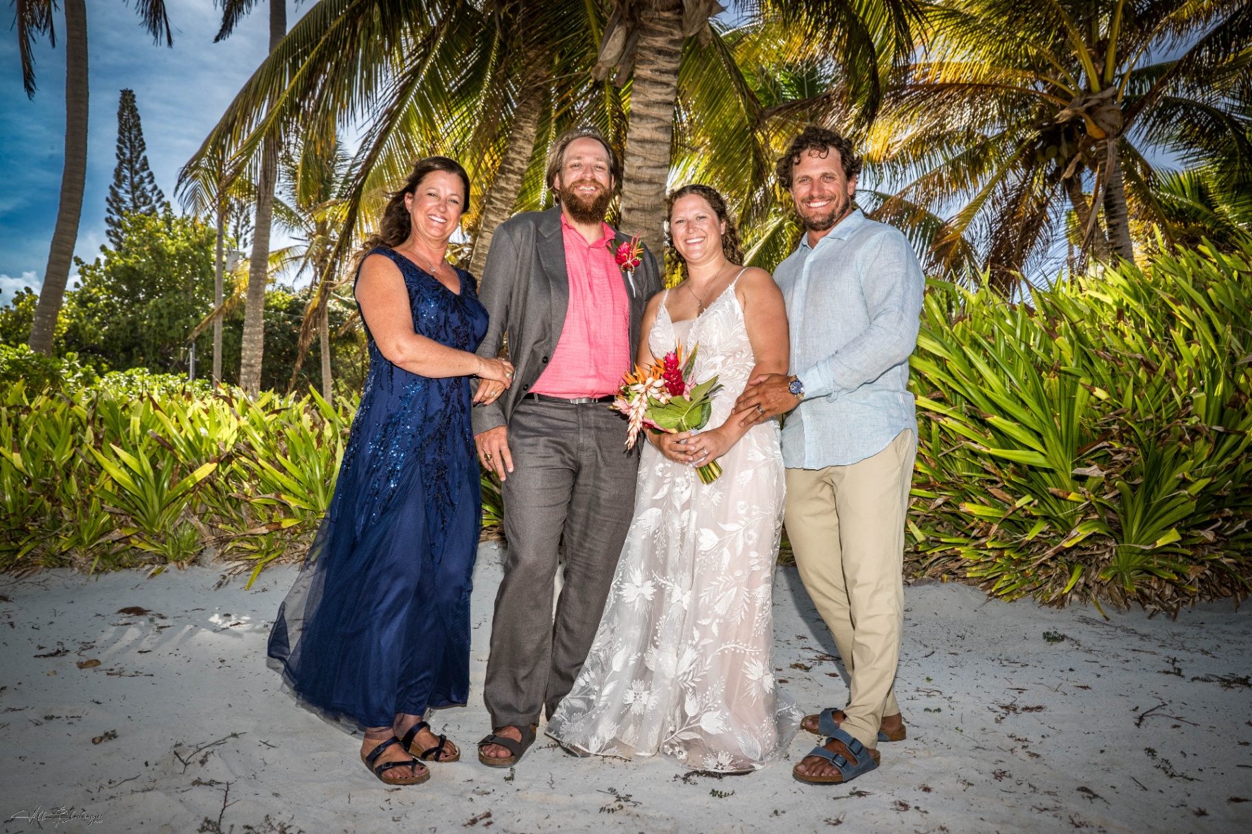 Bride and groom posing with both sets of parents on the white sand beach