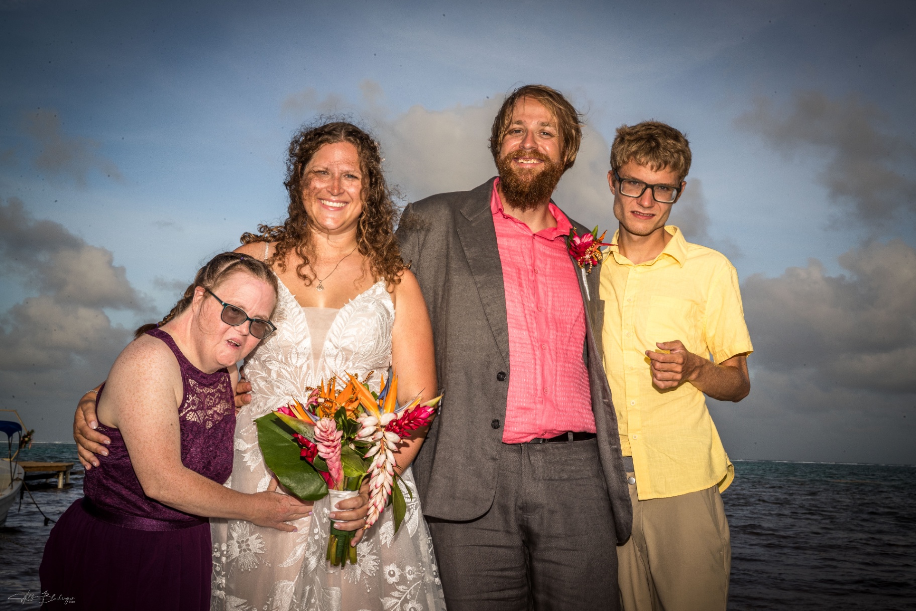 Bride and groom posing with two younger family members beside the water after the ceremony