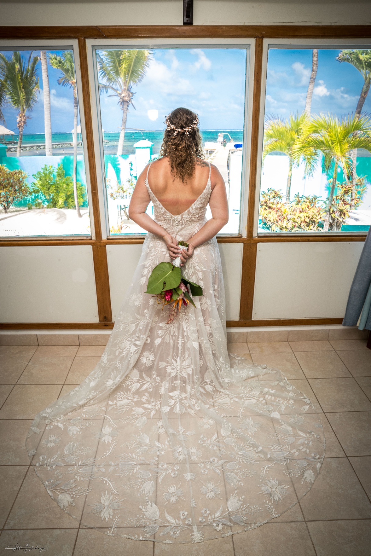Back view of the bride's lace dress and long train as she looks out toward the Caribbean