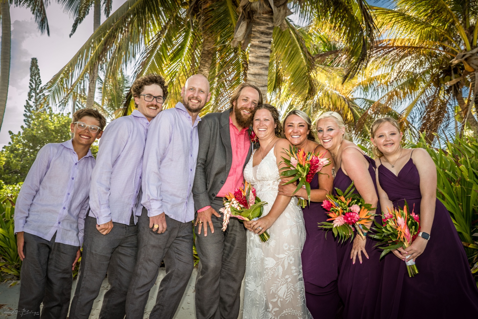 The full wedding party laughing together beneath the palms after the ceremony