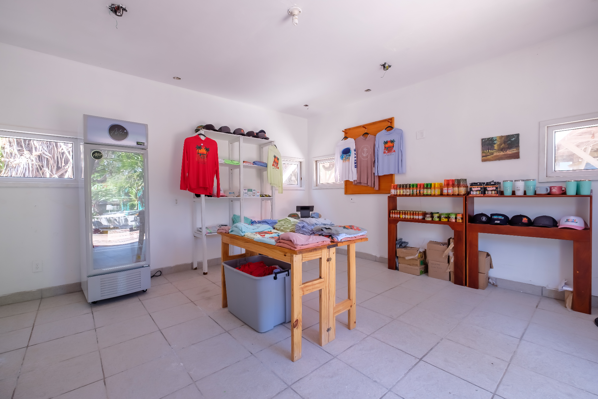 Gift shop interior with apparel rack, cooler, hot sauces, and Belize-branded mugs and caps