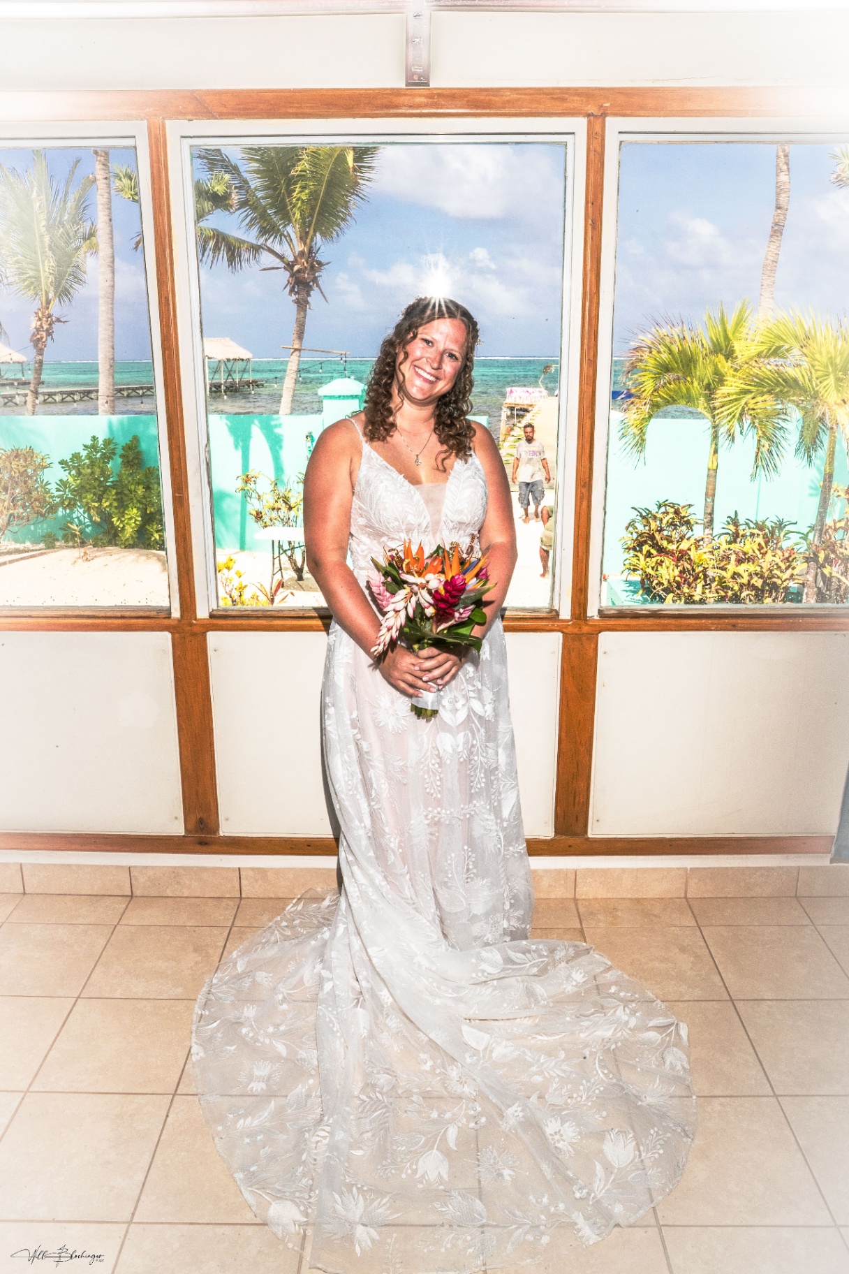 Bride posing with her bouquet in front of large windows overlooking the Playa Blanca beach