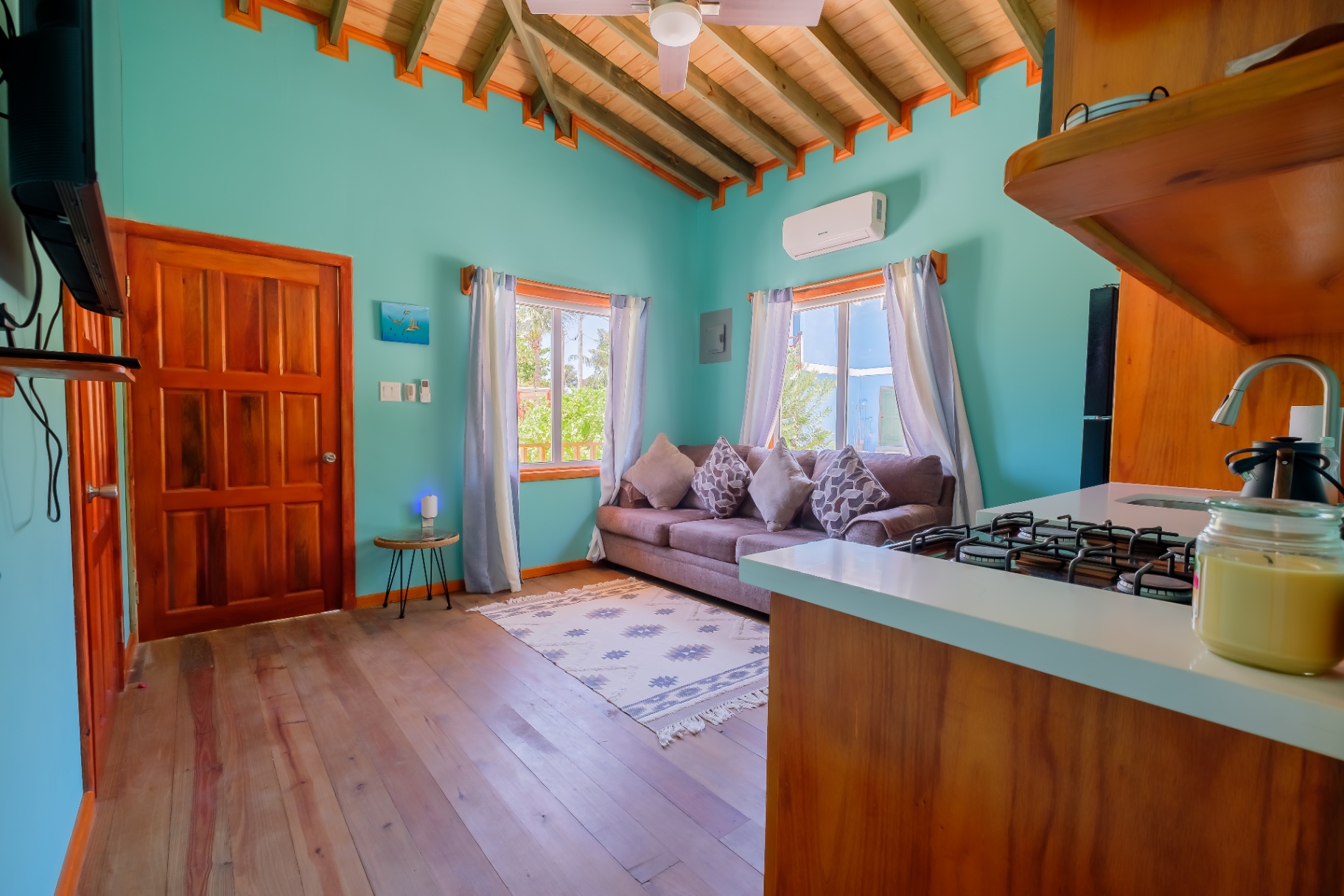Living room entry with vaulted beam ceiling, sofa, and kitchen bar